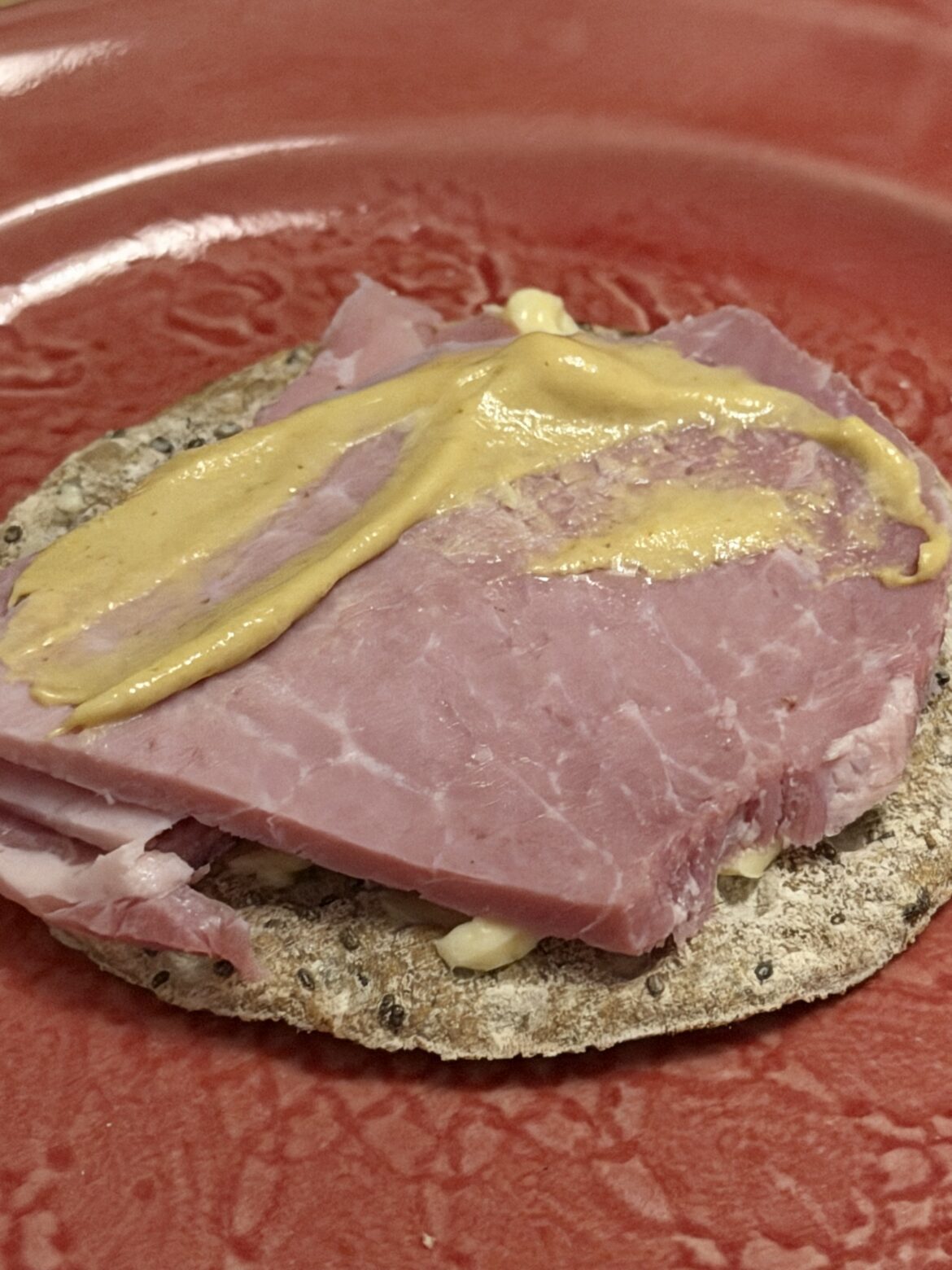 En hårdbrödsmörgås med julskinka och senap på en rosa tallrik