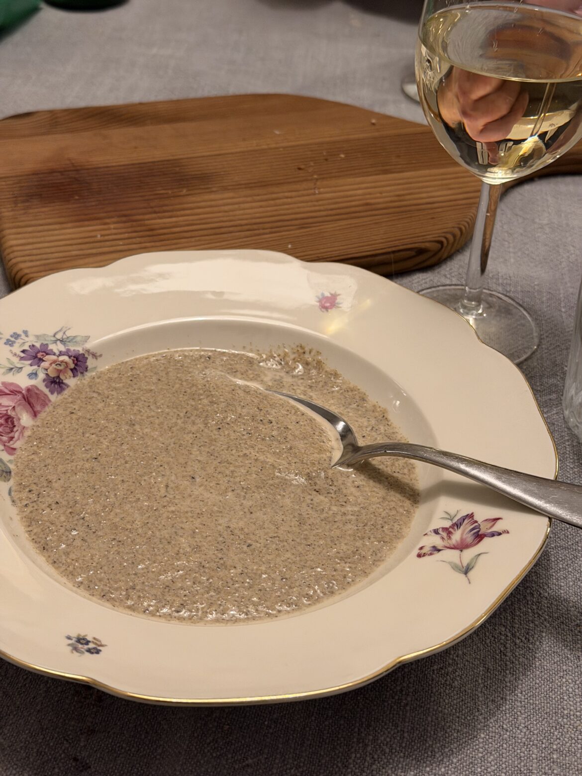 Krämig trattkantarellsoppa i en blommig porslinstallrik med sked, bredvid ett glas vitt vin.